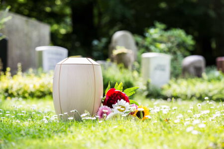 Holzurne mit bunten Blumen auf dem Friedhof