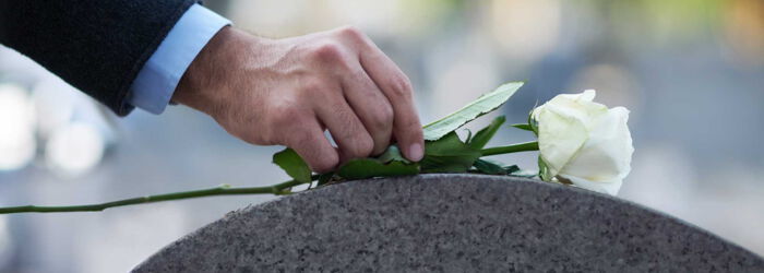 Mann legt weiße Rose auf Grabstein